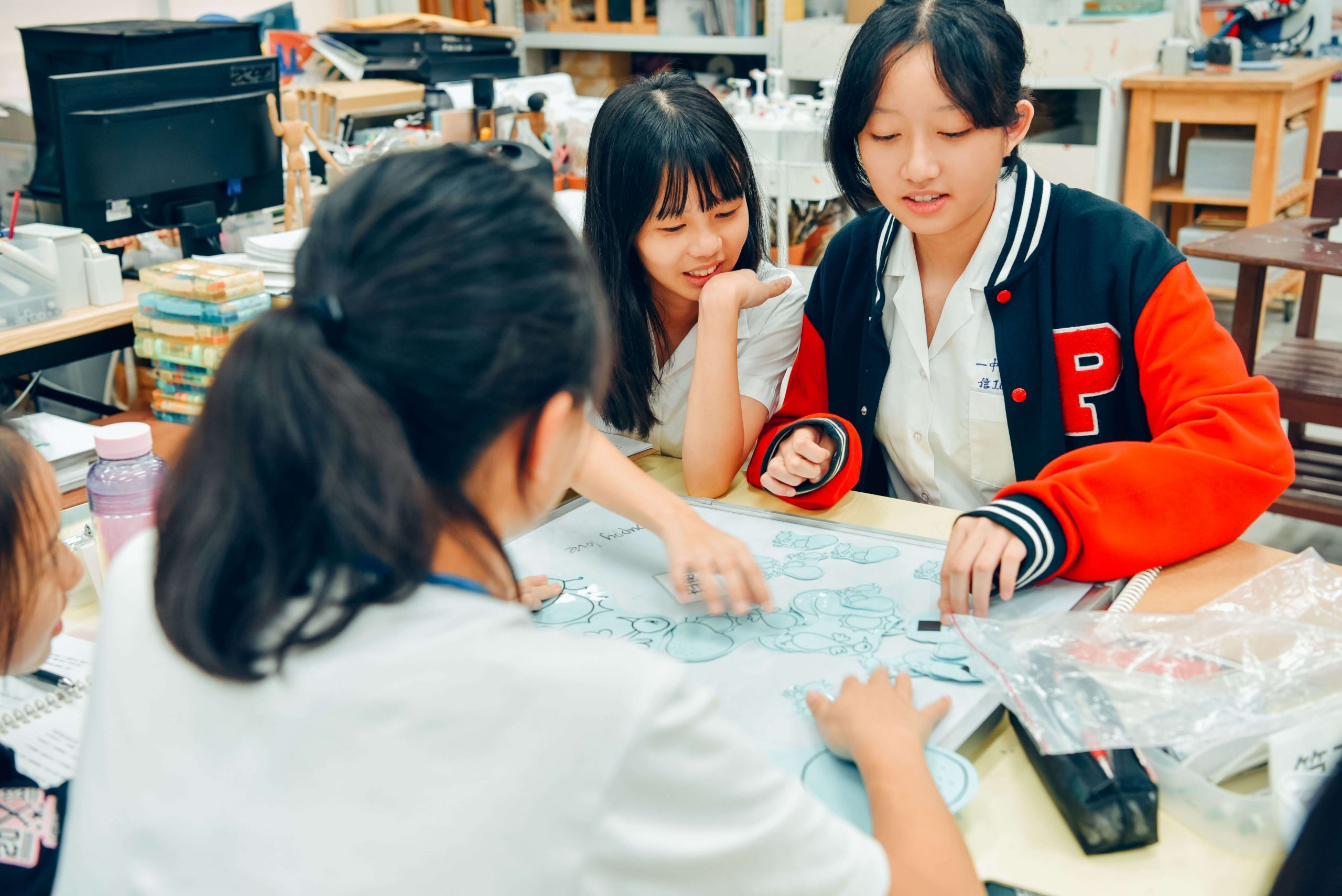 四位女同學在桌面上討論如何在白板上排版圖樣