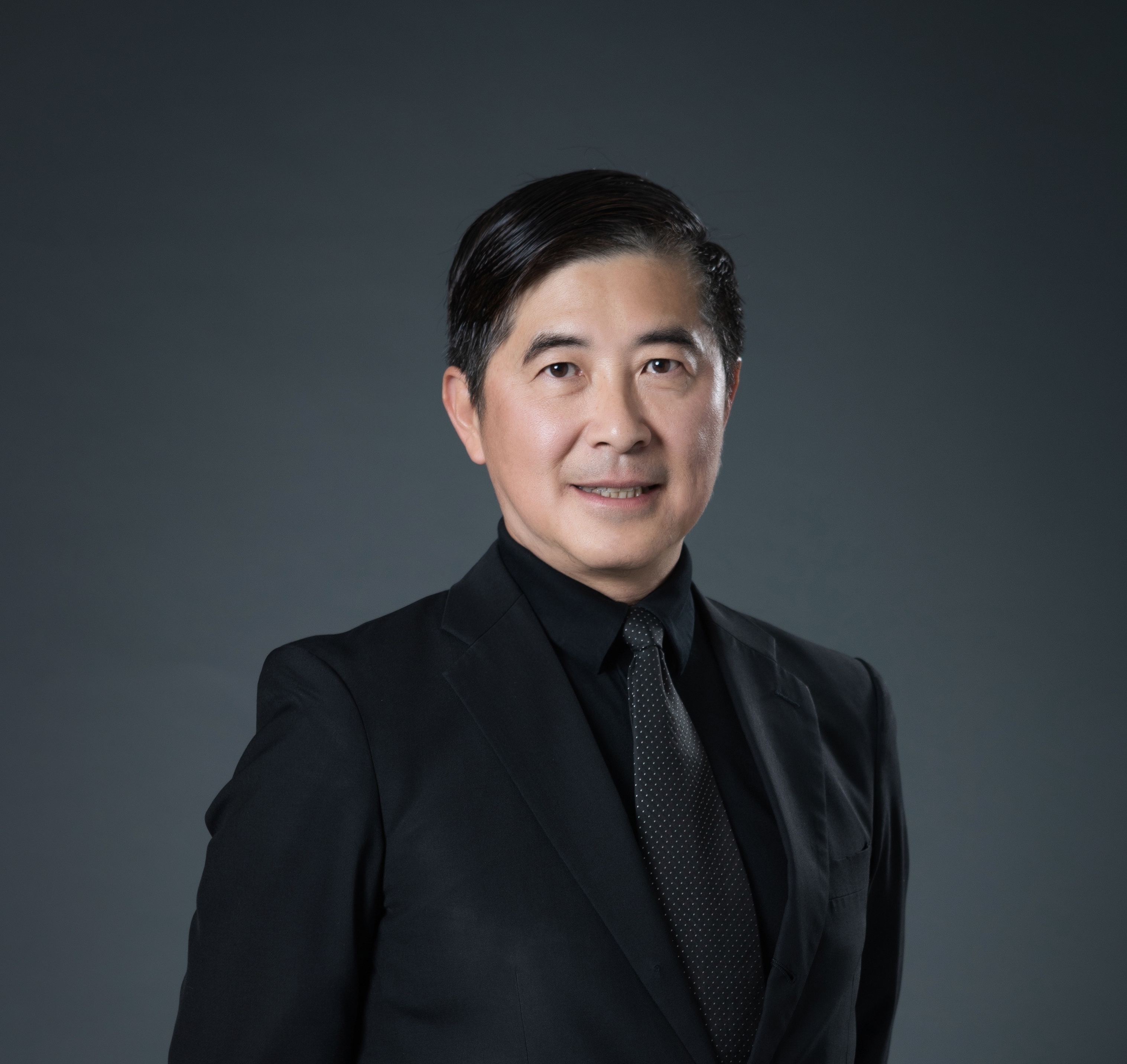 張基義老師著黑色西裝面帶笑容在黑色背景拍攝個人照